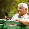 Happy senior man text messaging using mobile phone at park